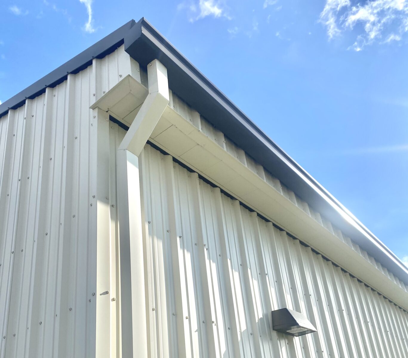 The image shows the corner of a metal building with a clear blue sky and a few clouds in the background.