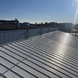 A sunlit metal roof with surrounding industrial buildings and solar panels under a clear blue sky.
