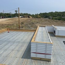 Construction site with steel beams installed on a foundation. Earth moving equipment visible in the background.